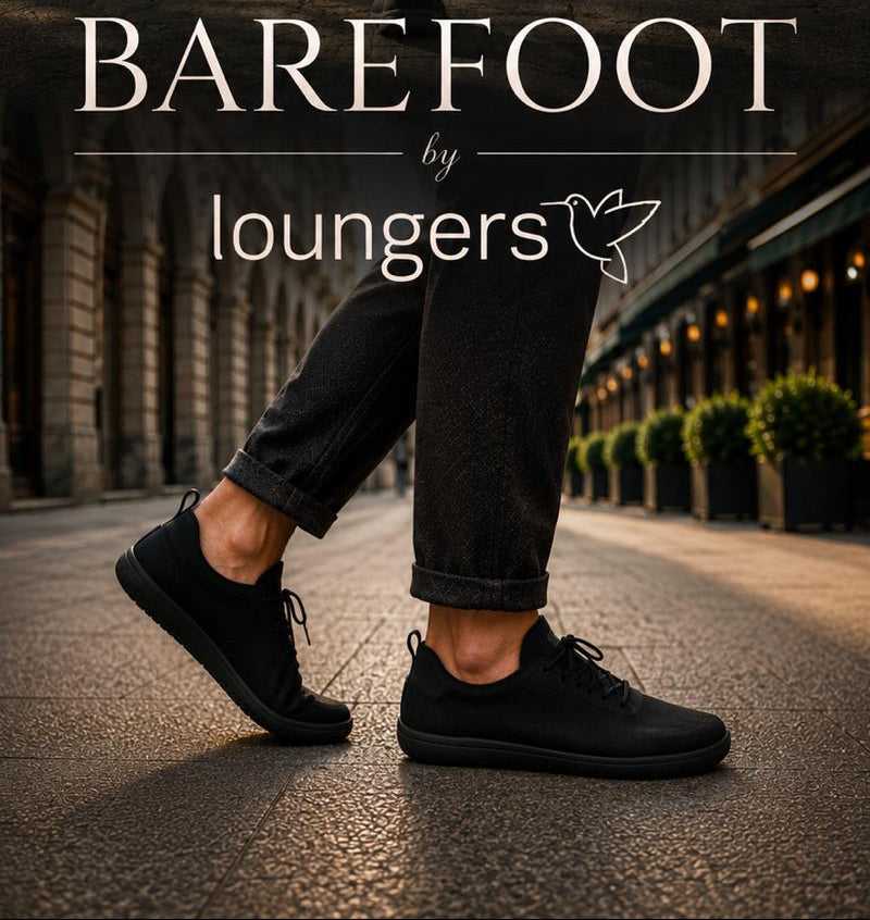 A man running down a tree-lined path wearing a black athletic t-shirt, black shorts, and black running shoes, with another person's legs in black jeans and black shoes in the foreground. Large text overlay reads 'BAREFOOT by loungers'.