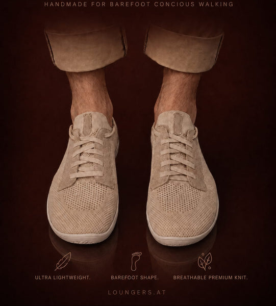 A pair of beige knit lounge sneakers shown on a person's bare feet, with rolled-up tan pants visible against a dark brown background. Large text at the top reads 'LOUNGERS' and smaller text includes 'HANDMADE FOR BAREFOOT CONCIUS WALKING' and feature callouts near the bottom.